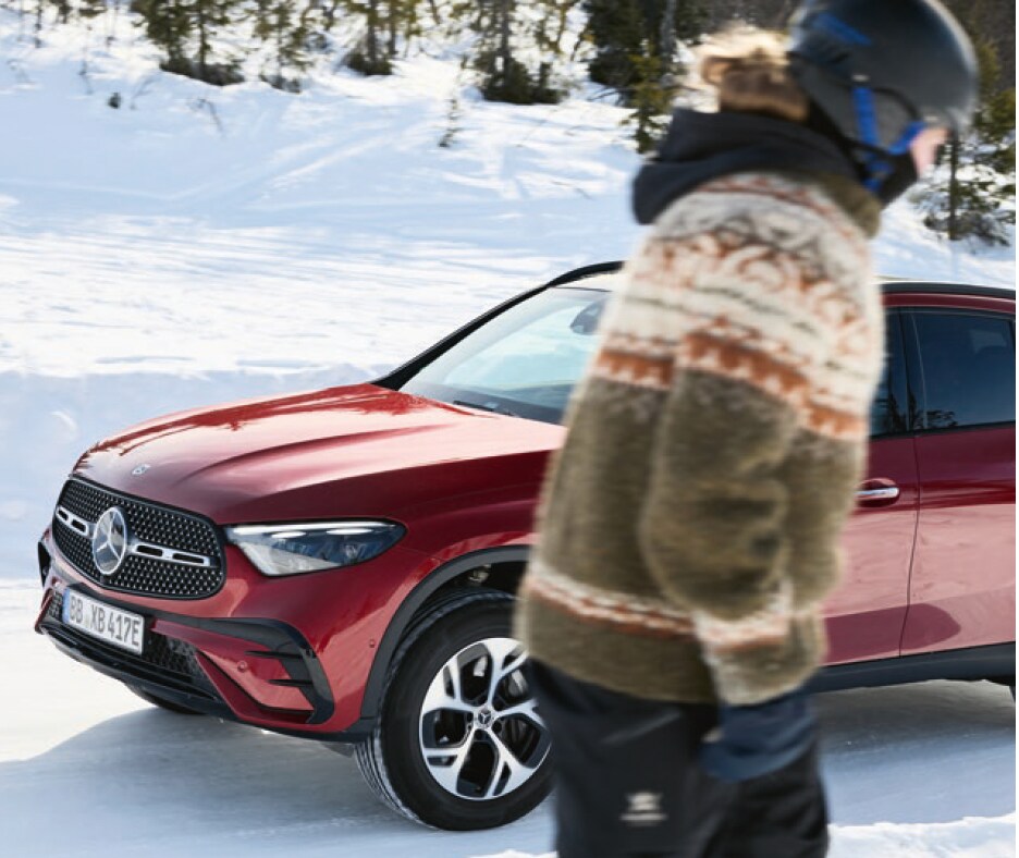 Klar til en sikker vinter. Rød Mercedes-Benz parkeret i sneklædt vinterlandskab, mens skiløber passerer
