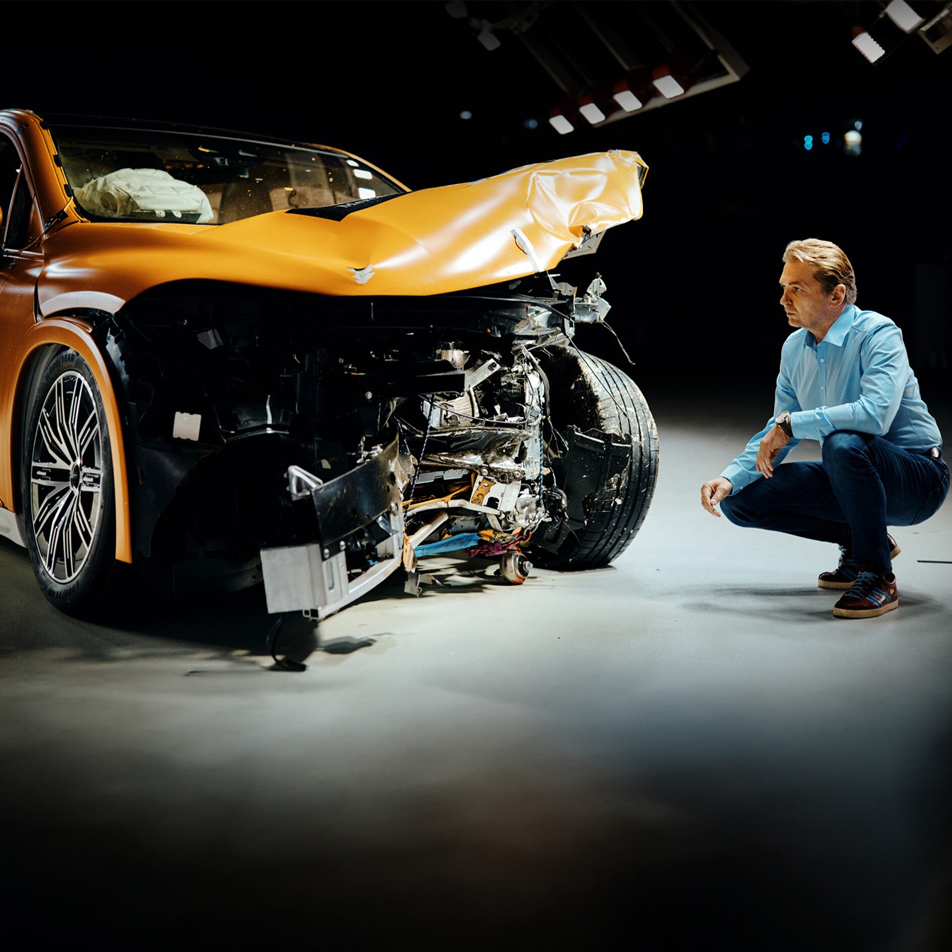 Kollisionstesteksperter | Sikkerhed | Mercedes-Benz Kollisionstestekspert undersøger en forulykket Mercedes-Benz bil, mens han sidder på hug ved siden af den.
